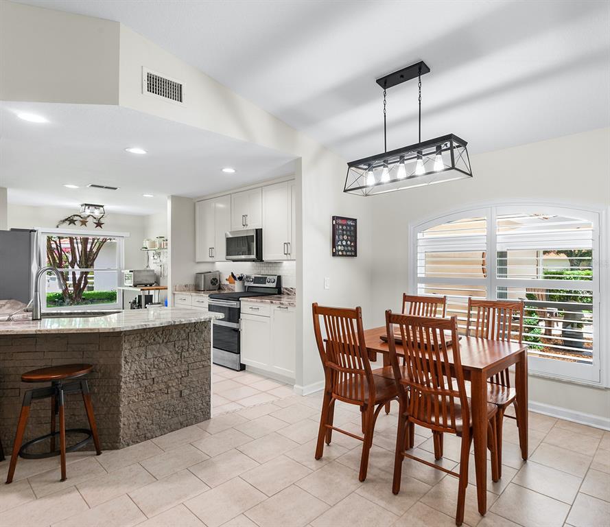 A kitchen with a stone-front island and a dining area featuring a wooden table set — 120 MORNING GLORY CIRCLE, WINTER HAVEN, FL