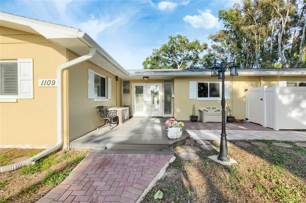 A single-story house exterior features a brick walkway, a wooden deck, and double glass doors — 1109 S SAN REMO AVENUE, CLEARWATER, FL