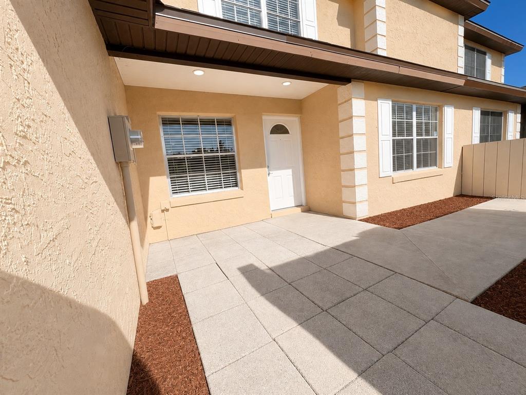 A beige stucco house exterior features a white front door and a paved patio area — 1255 SOPHIE BOULEVARD, ORLANDO, FL