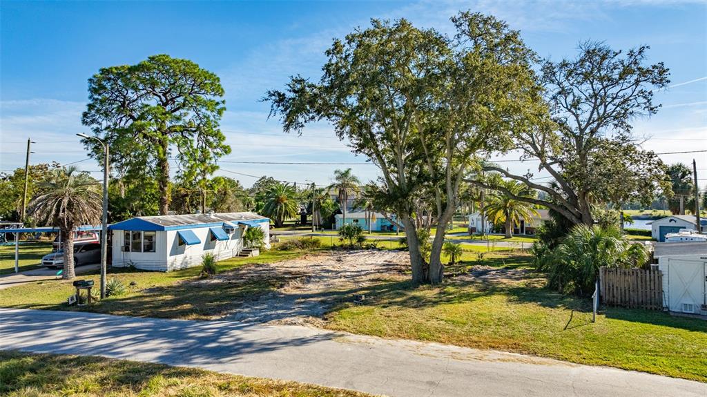 A vacant, sandy lot sits between a mobile home and a shed under large trees — 4836 SNUG HARBOR ROAD, NEW PORT RICHEY, FL
