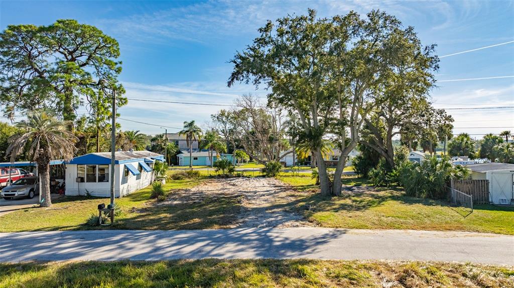 A vacant, sandy lot sits between a mobile home and a small shed under trees — 4836 SNUG HARBOR ROAD, NEW PORT RICHEY, FL