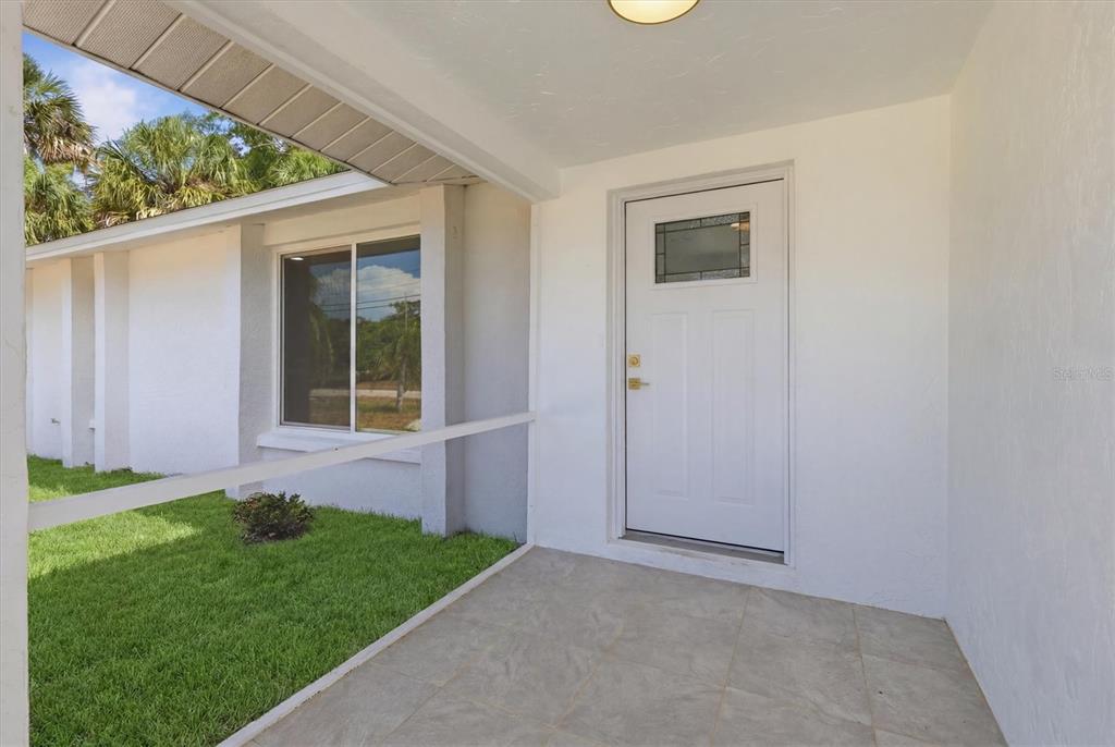 A white front door opens onto a tiled porch next to a grassy yard — 432 OLIVIA ROAD, VENICE, FL