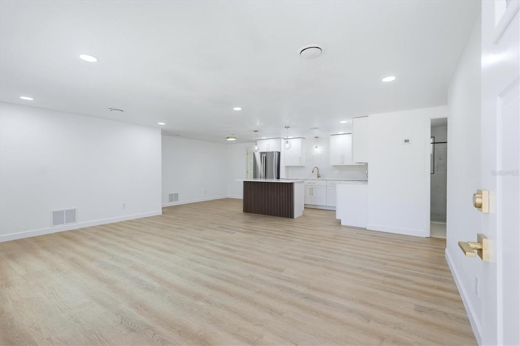 An open-concept living area features light wood-look flooring, white walls, and a modern kitchen island — 432 OLIVIA ROAD, VENICE, FL