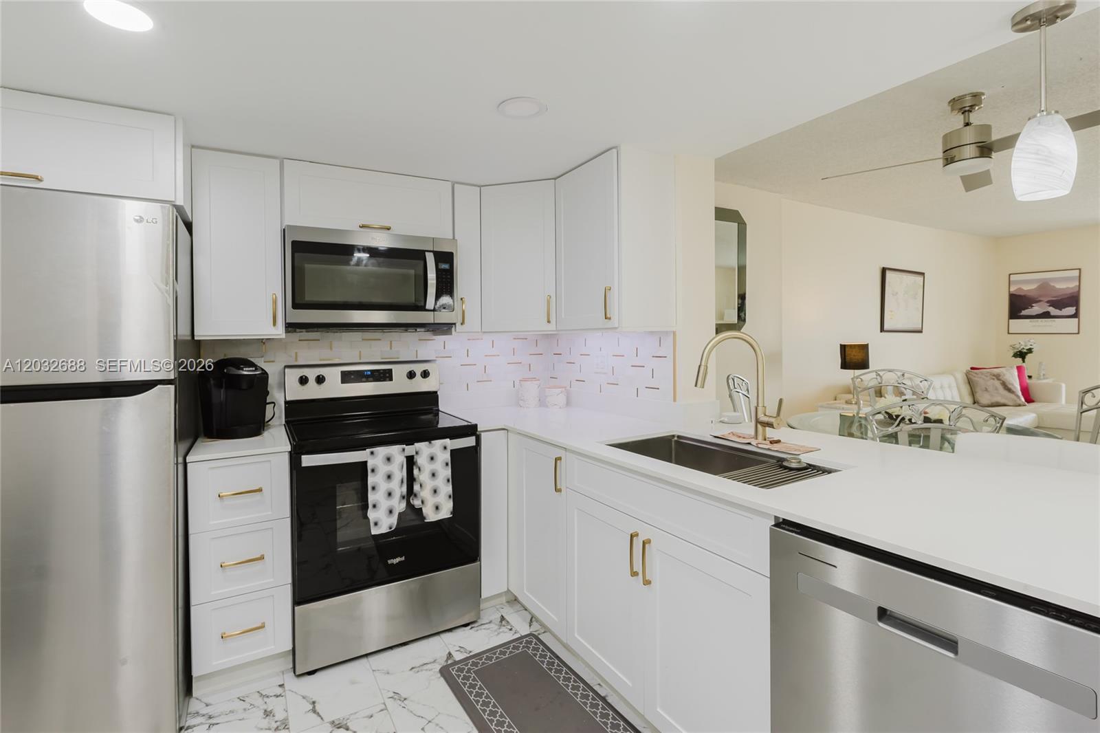A modern kitchen features white cabinets, stainless steel appliances, gold hardware, and marble-patterned tile flooring — 424 SE 10th St # 204, Dania Beach FL 33004, DANIA BEACH, FL