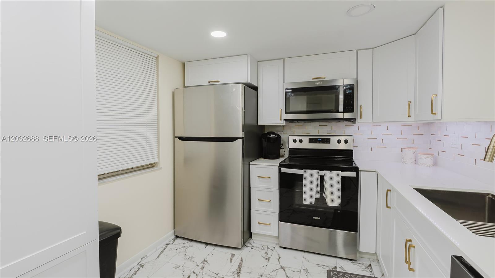 A kitchen features white cabinets, stainless steel appliances, and white marble-patterned tile flooring — 424 SE 10th St # 204, Dania Beach FL 33004, DANIA BEACH, FL