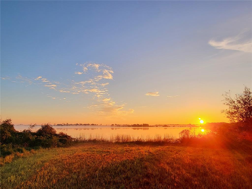 A sunrise over a calm lake with a grassy foreground and distant treeline — 960 ALBRITTON WAY, LAKE WALES, FL
