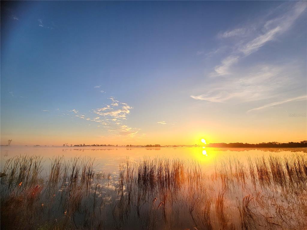 A sunrise over a calm lake with tall grasses in the foreground — 960 ALBRITTON WAY, LAKE WALES, FL