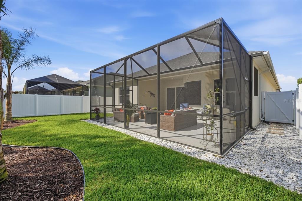 A screened-in patio with outdoor furniture sits in a backyard with a white vinyl fence — 24 SPRING STREET, PALM COAST, FL