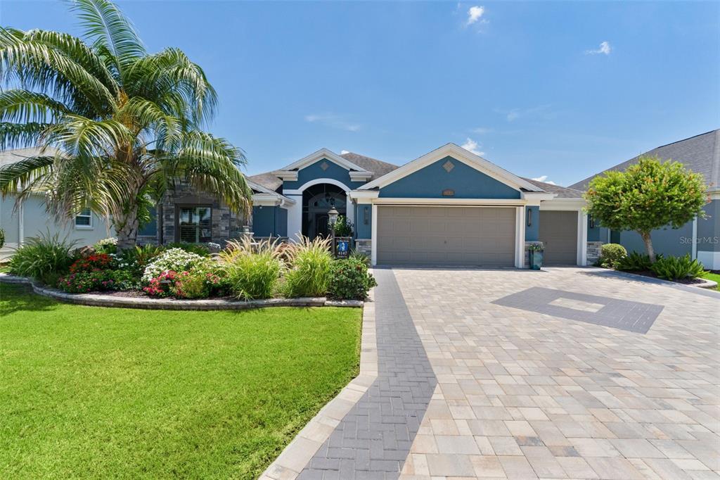 A blue house with a stone facade, a paved driveway, and a palm tree — 4147 DESKIN LANE, THE VILLAGES, FL