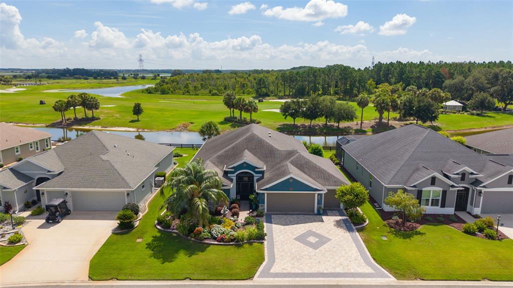 An aerial view shows three suburban houses with paved driveways facing a golf course — 4147 DESKIN LANE, THE VILLAGES, FL