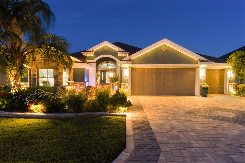 A single-story house with a paved driveway, green exterior walls, and illuminated landscaping at dusk — 4147 DESKIN LANE, THE VILLAGES, FL