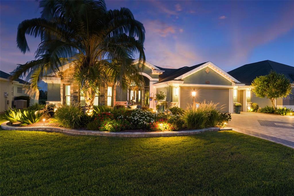 A single-story house with a stone facade, palm tree, and landscaped garden at twilight — 4147 DESKIN LANE, THE VILLAGES, FL