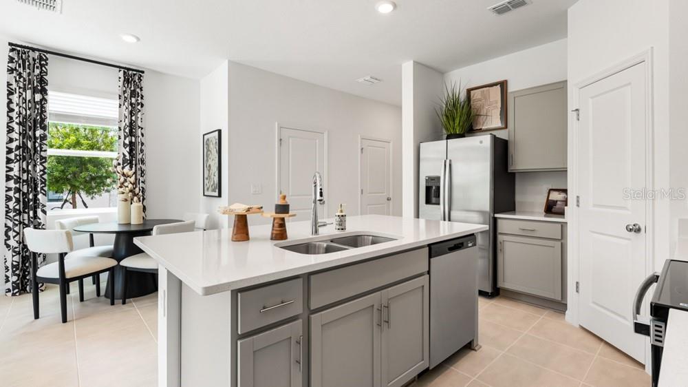A kitchen features a central island with a sink, stainless steel appliances, and gray cabinetry — 7167 GRAND FOREST WAY, NOKOMIS, FL