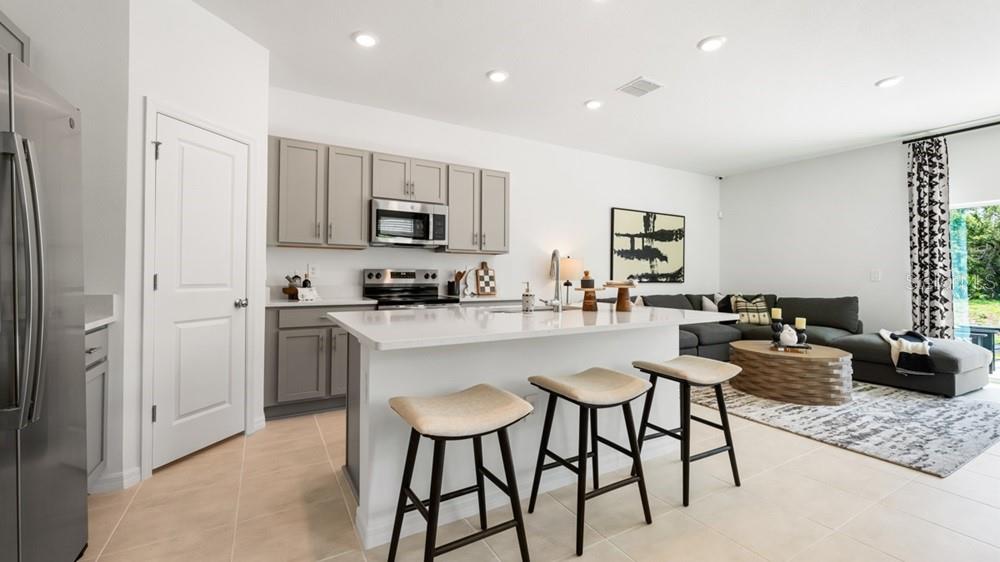 A modern kitchen with gray cabinets and a white island opens into a living area — 7167 GRAND FOREST WAY, NOKOMIS, FL