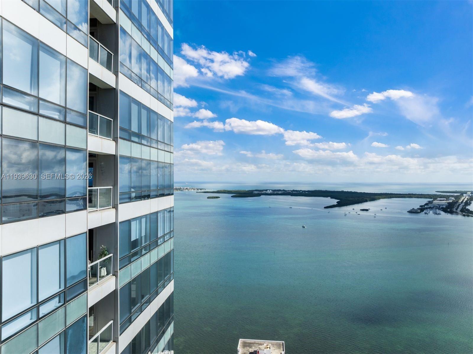 An exterior view of a high-rise building overlooking a large bay and distant land — 1425 Brickell Ave # 56F, Miami FL 33131, MIAMI, FL