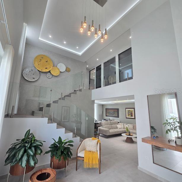 A modern living room features a floating staircase, glass railings, and a multi-pendant light fixture — 1 RUBI, VEGA ALTA, PR