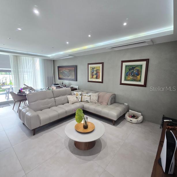 A modern living room features a large light-gray sectional sofa, a round coffee table, and artwork — 1 RUBI, VEGA ALTA, PR