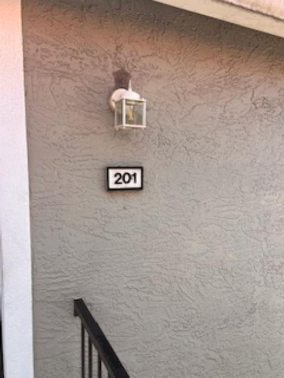 A wall-mounted outdoor light fixture hangs above a sign displaying the number 201 — 1149 EXCELLER COURT UNIT 201, CASSELBERRY, FL