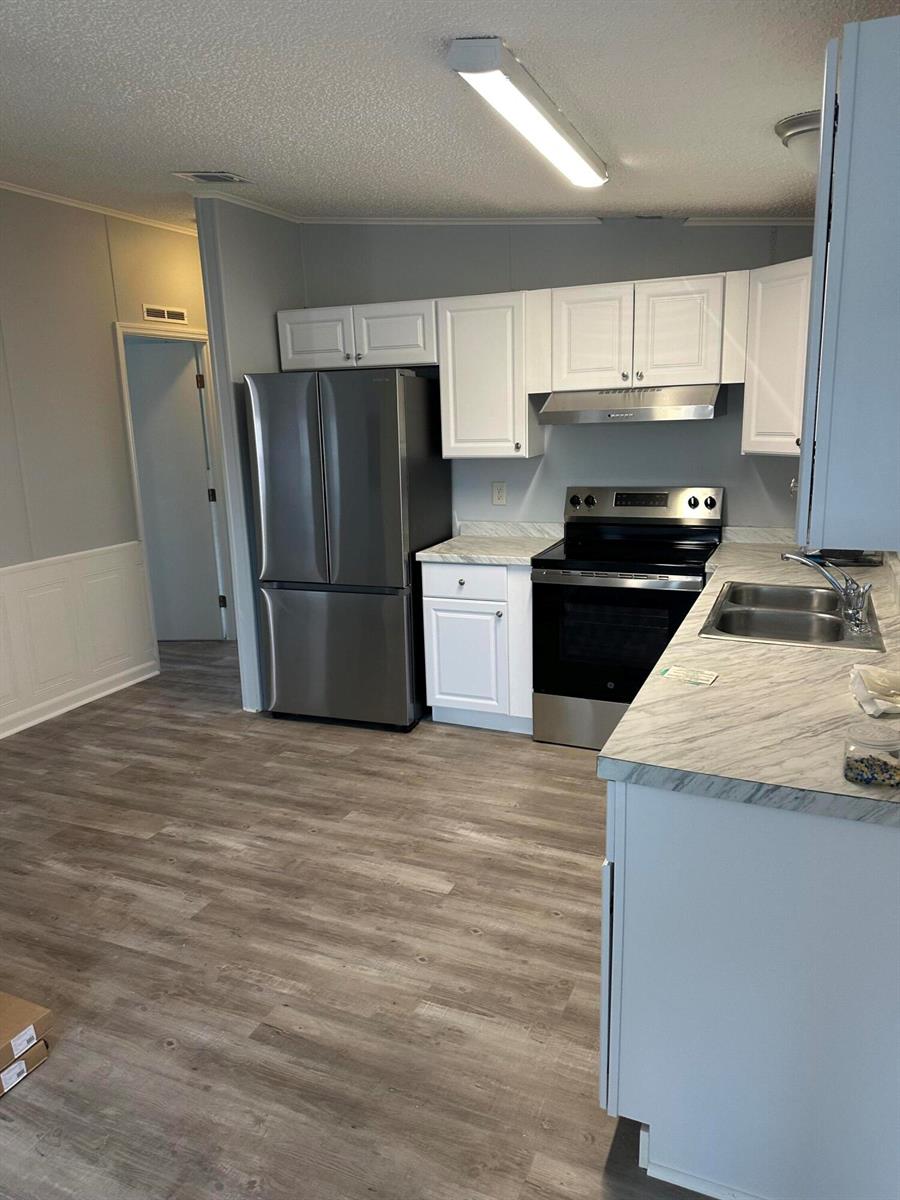 A kitchen features white cabinets, stainless steel appliances, and marble-patterned countertops over wood-look flooring — 528 Tropical Isles Circle, Fort Pierce FL 34982, FORT PIERCE, FL