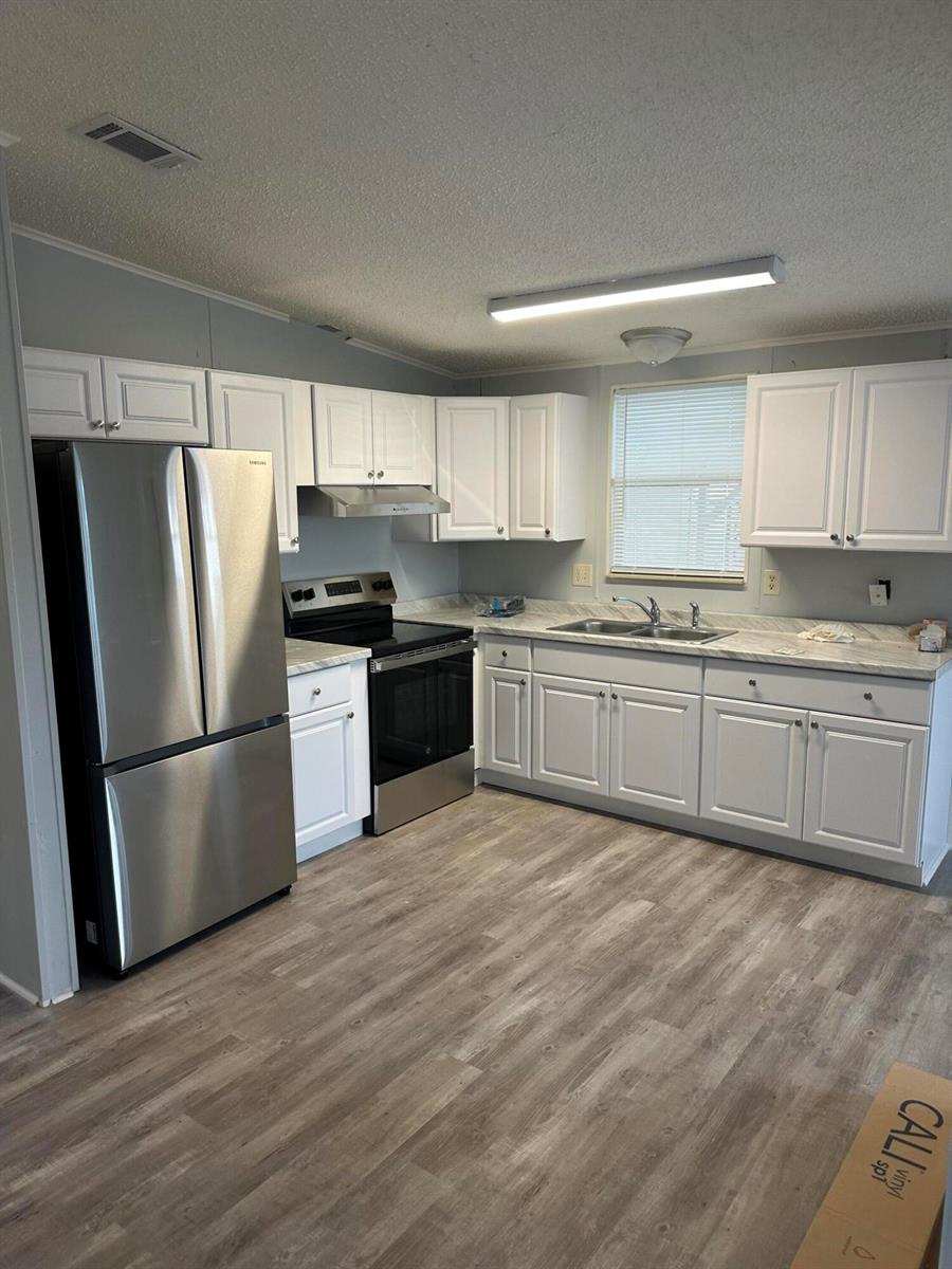 A kitchen features white cabinets, stainless steel appliances, a double sink, and wood-look flooring — 528 Tropical Isles Circle, Fort Pierce FL 34982, FORT PIERCE, FL