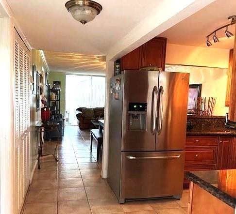 A kitchen with stainless steel appliances and wood cabinets leads into a tiled living area — 9350 Sunrise Lakes Boulevard # 101, Sunrise FL 33322, SUNRISE, FL