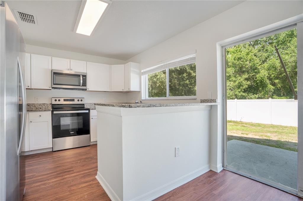 A kitchen features white cabinets, stainless steel appliances, granite countertops, and a sliding glass door — 10225 SUMMERVIEW CIRCLE, RIVERVIEW, FL