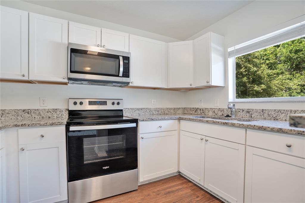 A kitchen features white cabinets, granite countertops, stainless steel appliances, and wood-look flooring — 10225 SUMMERVIEW CIRCLE, RIVERVIEW, FL