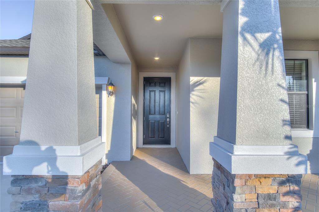 A covered entryway features a dark front door, stone-based columns, and a herringbone-patterned floor — 1212 MONTGOMERY BELL ROAD, WESLEY CHAPEL, FL
