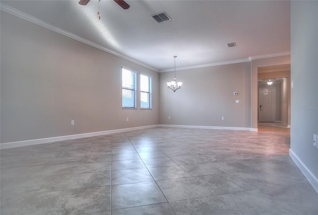 An empty room with gray tile flooring, light-colored walls, a chandelier, and a ceiling fan — 1212 MONTGOMERY BELL ROAD, WESLEY CHAPEL, FL