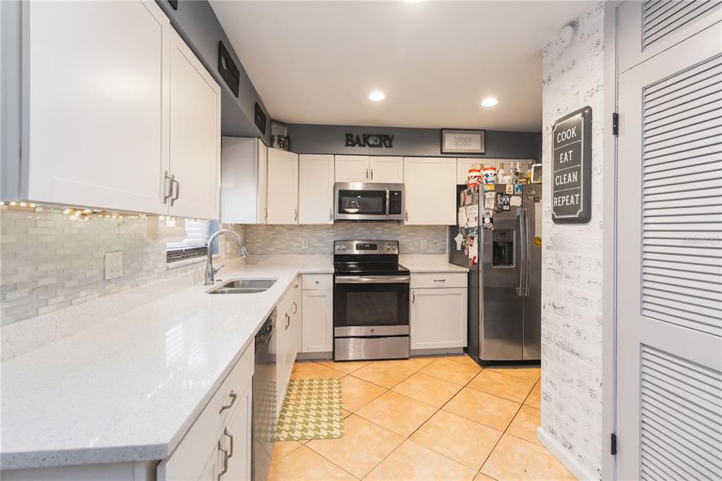 A kitchen features white cabinets, stainless steel appliances, quartz countertops, and light-colored tile flooring — 1624 BLOOMFIELD AVENUE, DELTONA, FL