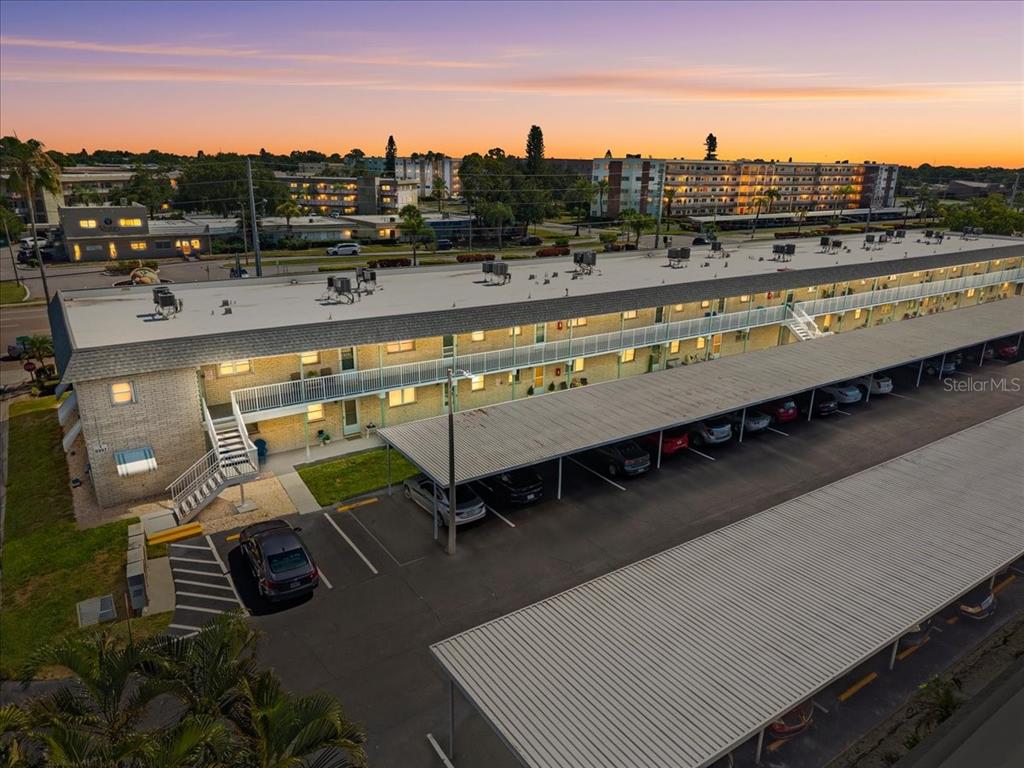 An aerial view of a multi-story apartment building with covered parking and a sunset sky — 5357 81ST STREET N UNIT 18, ST PETERSBURG, FL