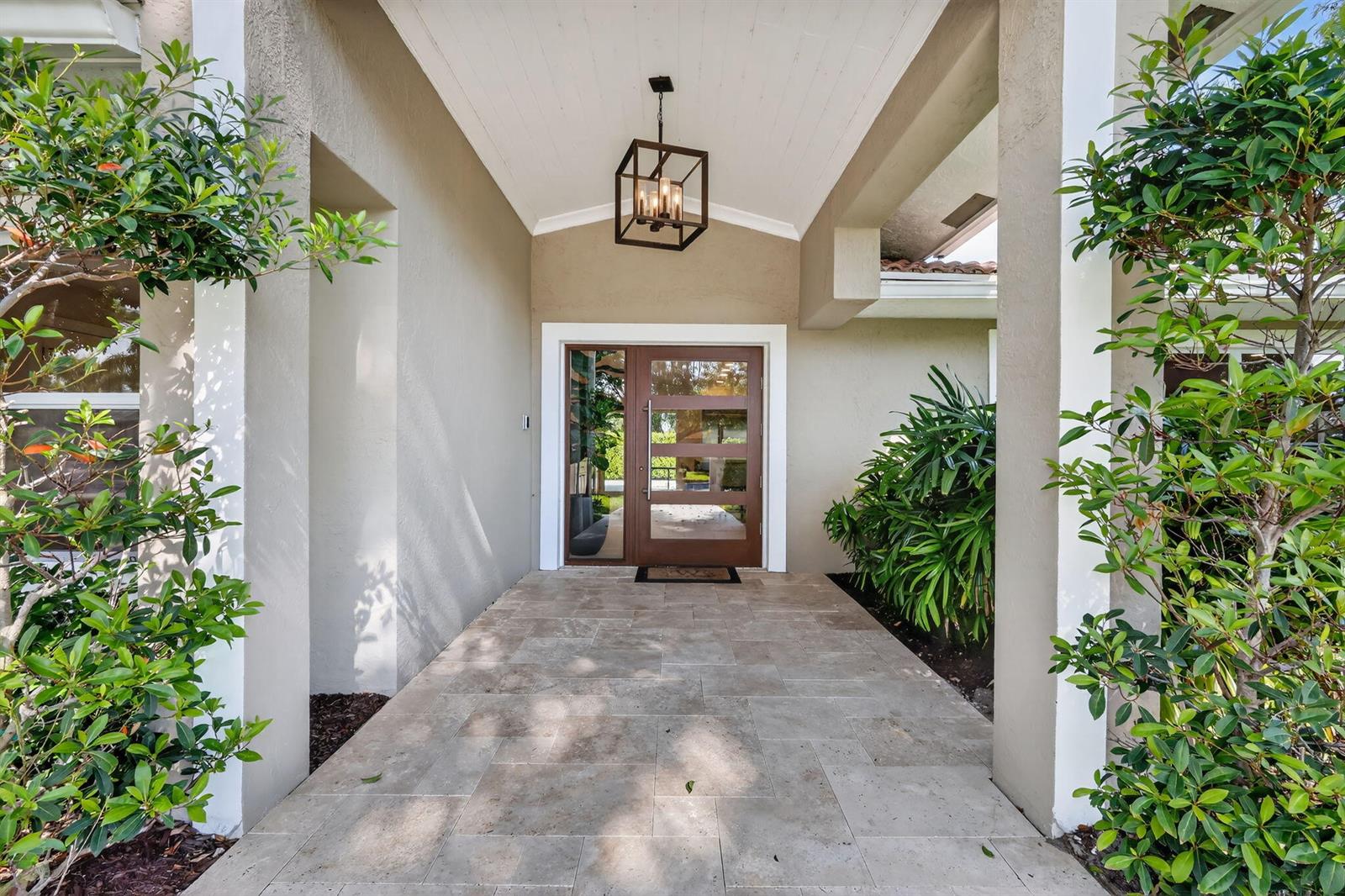 A covered entryway features a modern wood door, stone tile flooring, and a hanging lantern — 937 SW 34th Court, Boynton Beach FL 33435, BOYNTON BEACH, FL