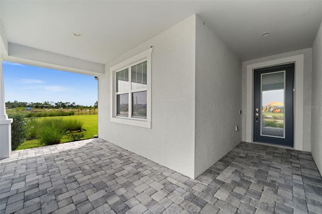 A covered patio with gray paver flooring, a white exterior wall, and a glass-paneled door — 15880 ELINA SKY DRIVE, PUNTA GORDA, FL