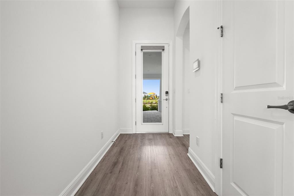 A hallway with wood-look flooring leads to a glass-paneled door showing an outdoor playground — 15880 ELINA SKY DRIVE, PUNTA GORDA, FL