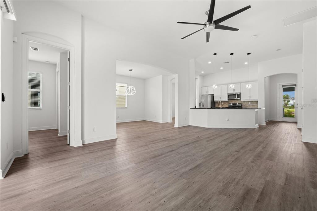An open-concept living area features light wood-look flooring, white walls, and an adjacent kitchen — 15880 ELINA SKY DRIVE, PUNTA GORDA, FL
