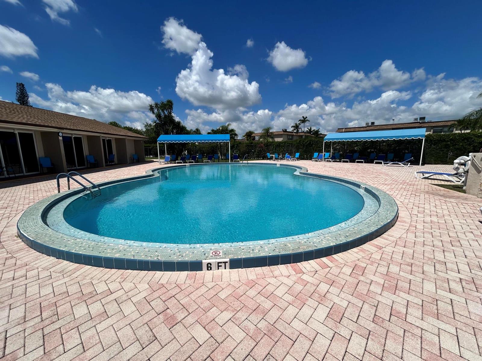 A kidney-shaped swimming pool with a brick paver deck and blue shade structures — 770 Lori Drive # 245, Palm Springs FL 33461, PALM SPRINGS, FL