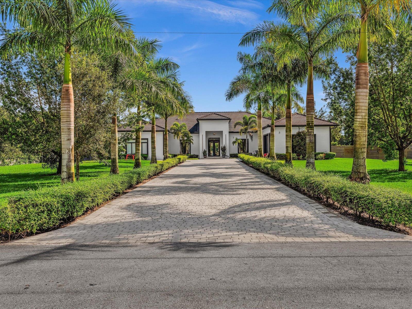 A paved driveway leads to a white house framed by palm trees and manicured hedges — SOUTHWEST RANCHES, FL