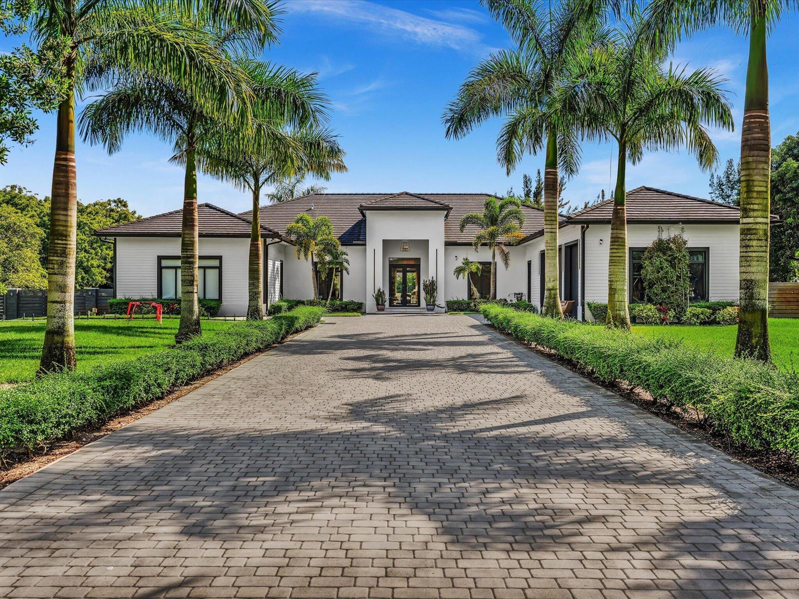 A paved driveway leads to the entrance of a white single-story house with palm trees — SOUTHWEST RANCHES, FL