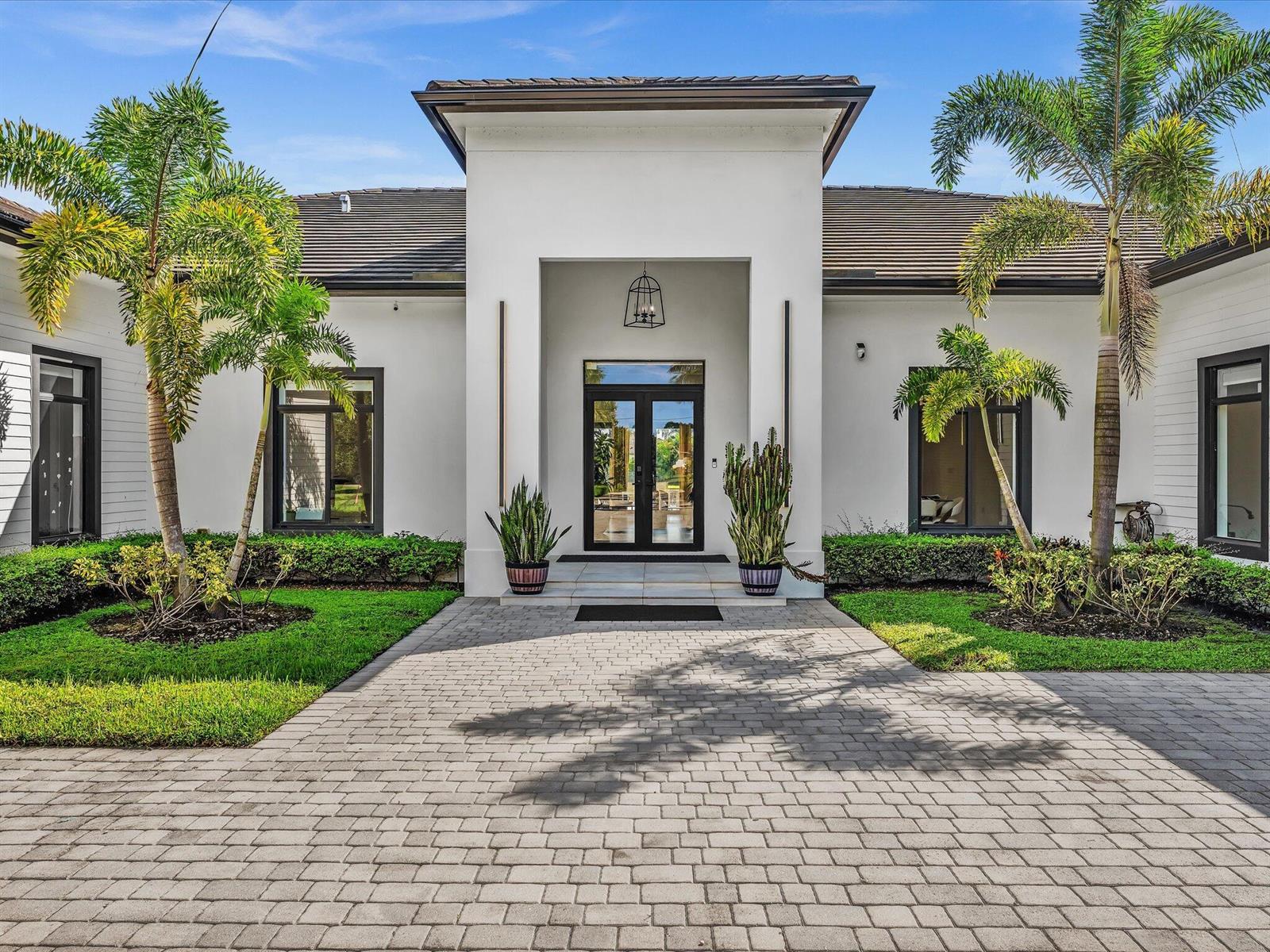 A modern white house with a paved driveway, palm trees, and a glass-paneled front door — SOUTHWEST RANCHES, FL