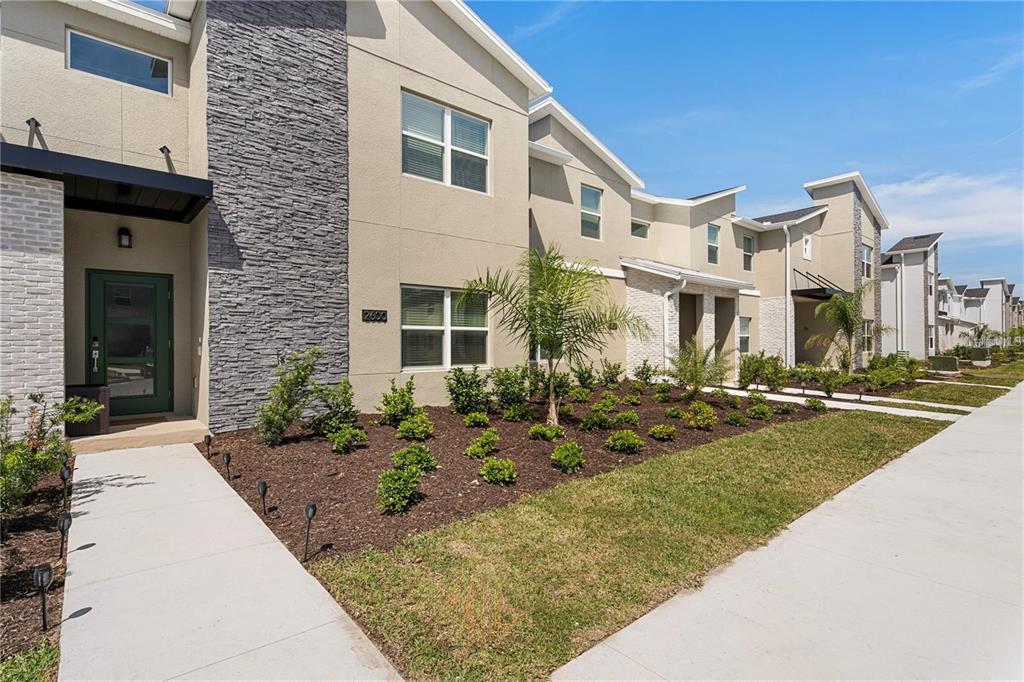 A modern multi-story townhouse exterior features a stone facade, a green door, and landscaping — 2600 READING TRAIL, KISSIMMEE, FL