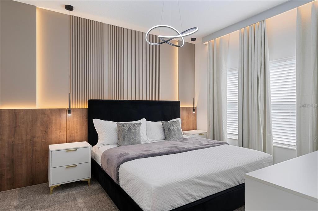 A bedroom features a black upholstered bed, wood-slat wall paneling with accent lighting, and pendant lights — 2600 READING TRAIL, KISSIMMEE, FL