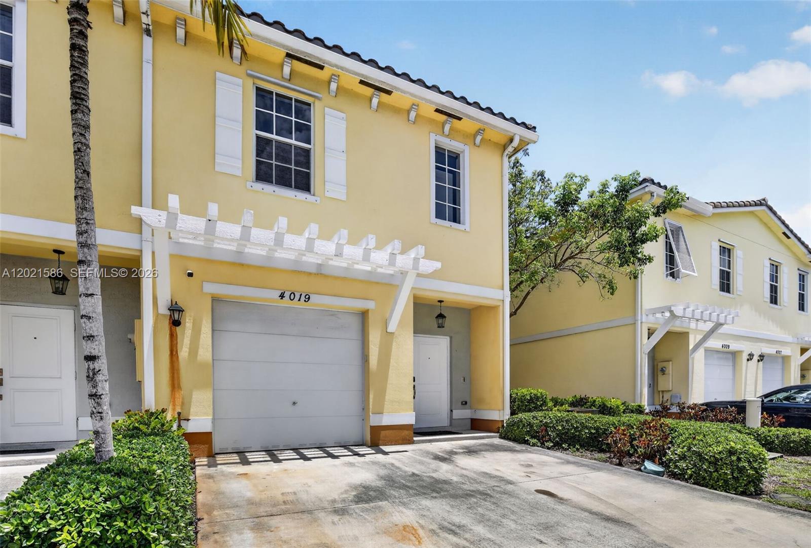 A yellow two-story townhouse features a garage, a white pergola, and a concrete driveway — 4019 NW 11th Dr, Lauderhill FL 33313, LAUDERHILL, FL