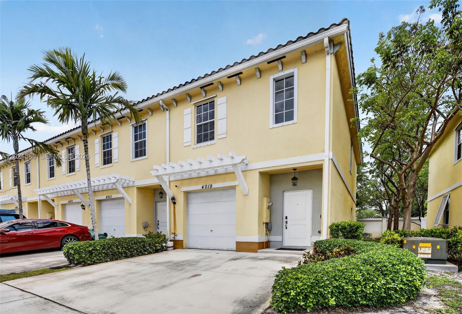 A yellow two-story townhouse features a white garage door, a front door, and landscaping — 4019 NW 11th Dr, Lauderhill FL 33313, LAUDERHILL, FL