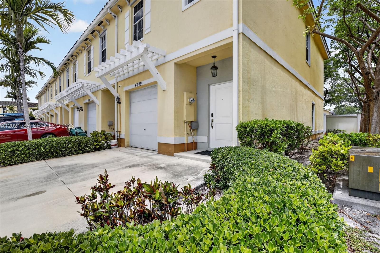 A yellow two-story townhouse features a white garage door, a front entrance, and landscaping — 4019 NW 11th Dr, Lauderhill FL 33313, LAUDERHILL, FL
