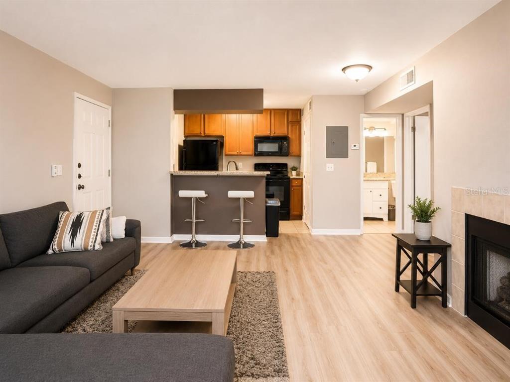 A living room with light wood flooring features a grey sofa, coffee table, and kitchen — 420 FORESTWAY CIRCLE UNIT 307, ALTAMONTE SPRINGS, FL
