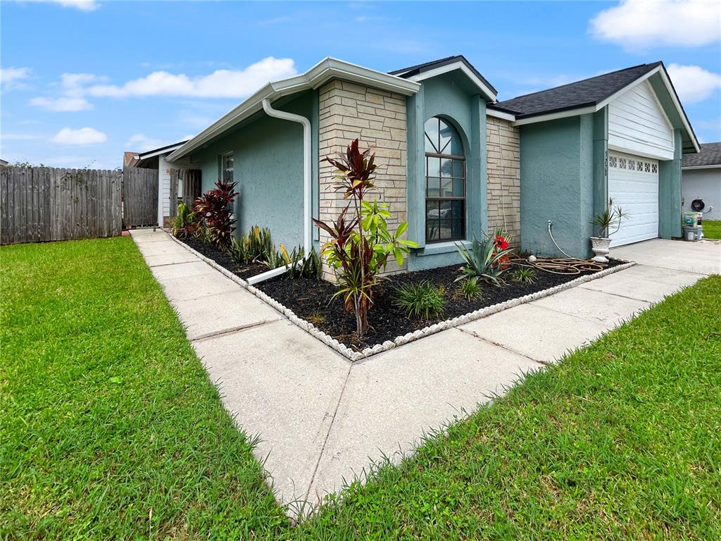 A teal house with stone accents, a concrete walkway, and a landscaped garden bed — 3228 RUNNING BEAR WAY, KISSIMMEE, FL