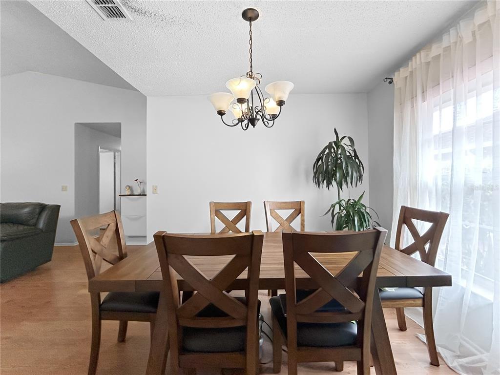 A dining room features a wooden table with chairs under a chandelier and sheer curtains — 3228 RUNNING BEAR WAY, KISSIMMEE, FL