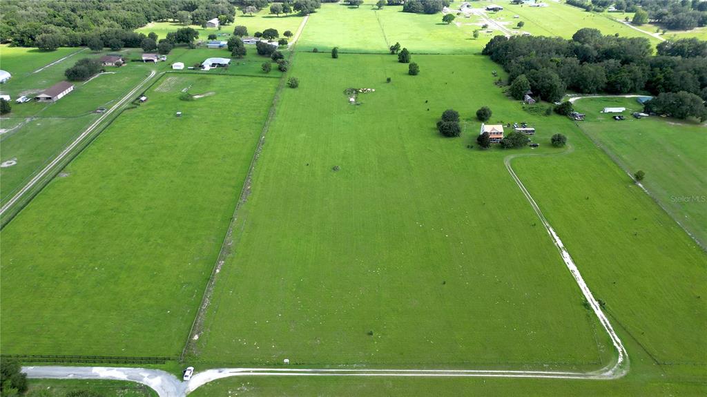 An aerial view shows a large, fenced green pasture with a house and several outbuildings — TBD SE 170TH STREET, WEIRSDALE, FL