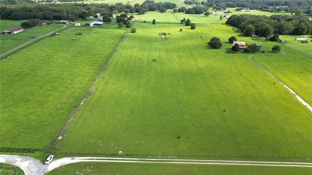 An aerial view shows a large, open green pasture with a house and surrounding trees — TBD SE 170TH STREET, WEIRSDALE, FL