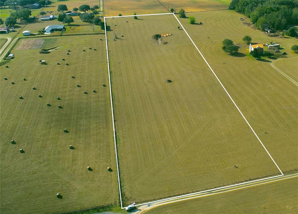 An aerial view shows a large, rectangular, fenced-in grassy field with scattered hay bales — TBD SE 170TH STREET, WEIRSDALE, FL